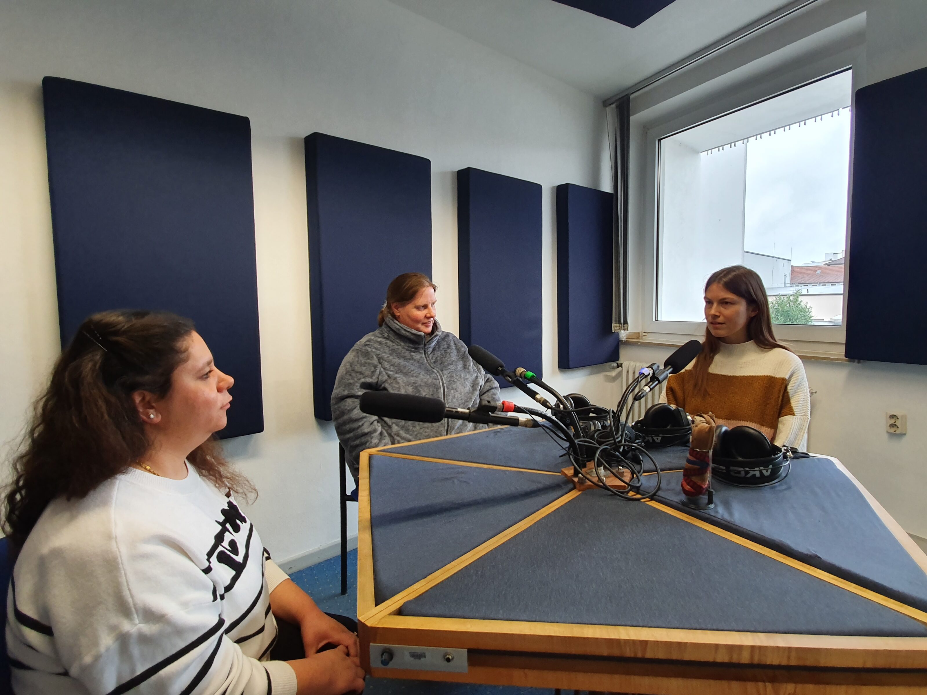 Drei Frauen sitzen in einem Tonstudio um den Tisch mit Mikrofonen.